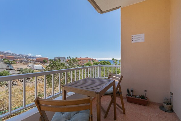 A balcony with a table and chairs, a potted plant, and a sign on the wall. - Brisas Del Mar Eddy: Mountain Views, Wi-Fi & Air Conditioning for Your Vacation (Candelaria)
