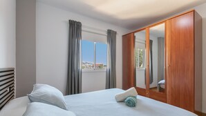 Habitación de hotel con cama, armario, ventana con cortinas y vistas al exterior.