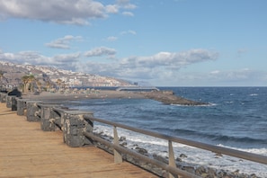 Un muelle de madera con barandillas de piedra que da a una playa con gente y palmeras.