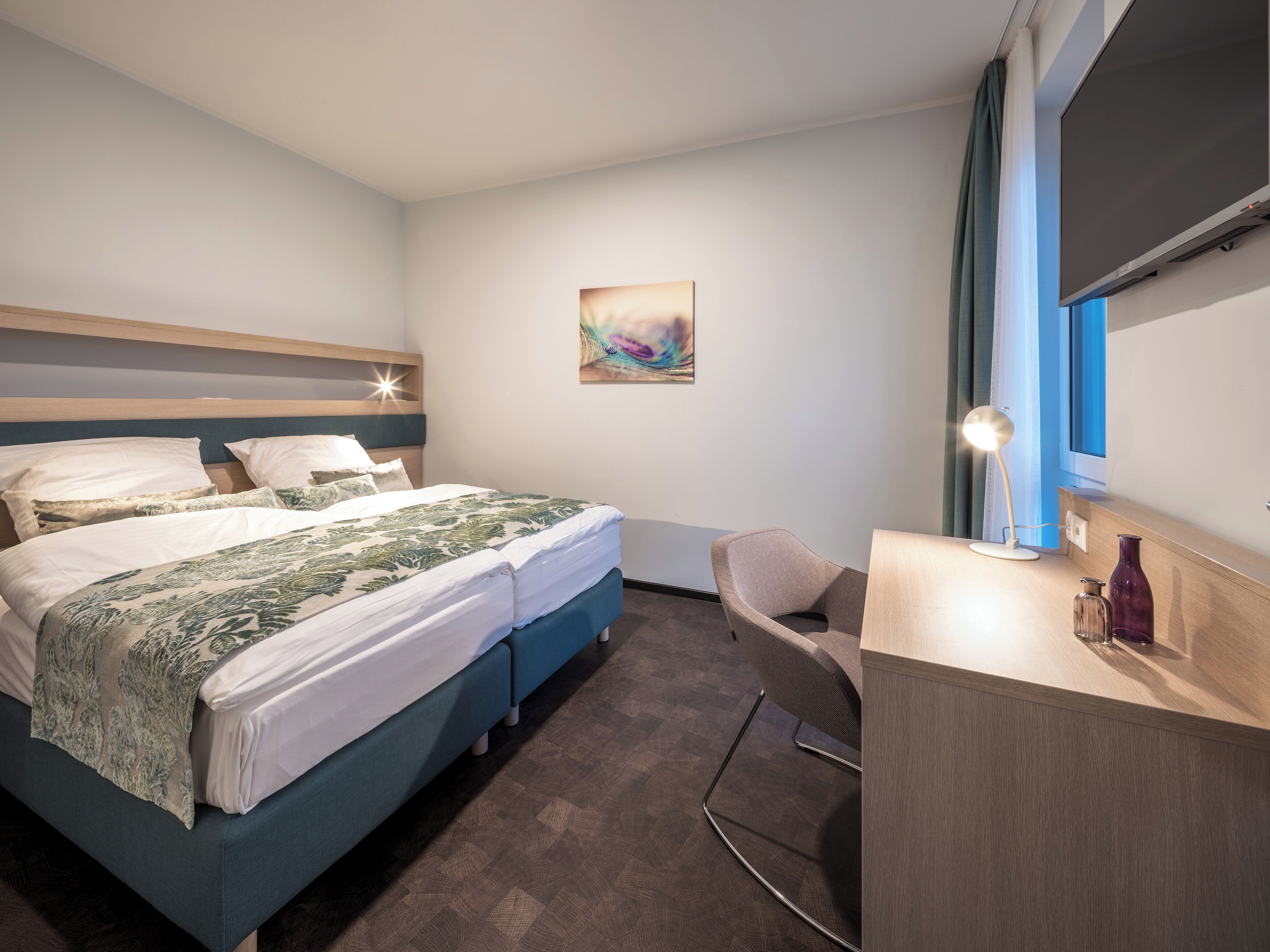 Une chambre d’hôtel moderne avec un lit, une table de chevet, une lampe et un tableau au mur.