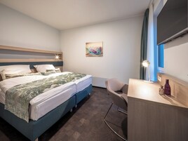 Une chambre d’hôtel moderne avec un lit, une table de chevet, une lampe et un tableau au mur.