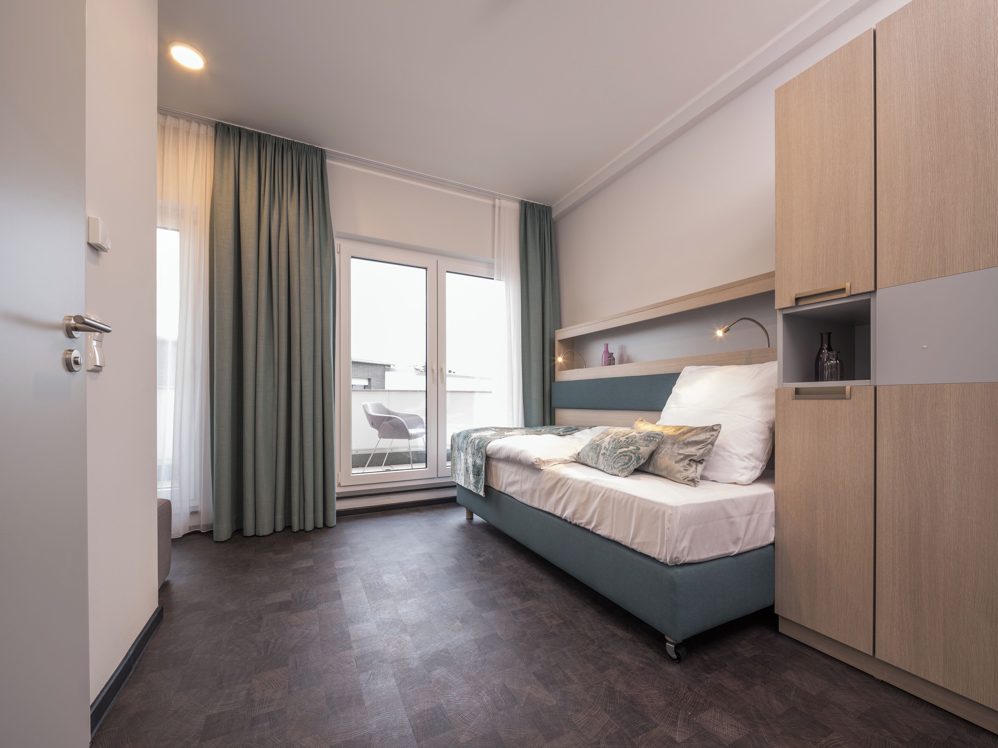 A modern bedroom with a bed, a wardrobe, and a sliding glass door to a balcony.