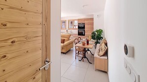 A modern kitchen with wooden cabinets, a dining area with a table and chairs, and a living area with a sofa and a plant. - Le Framiré-appartement-4pers-Proche piste (Les Gets)