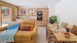 A modern kitchen with wooden cabinets, a dining table set for two, and a sofa with a blanket. - Le Framiré-appartement-4pers-Proche piste (Les Gets)