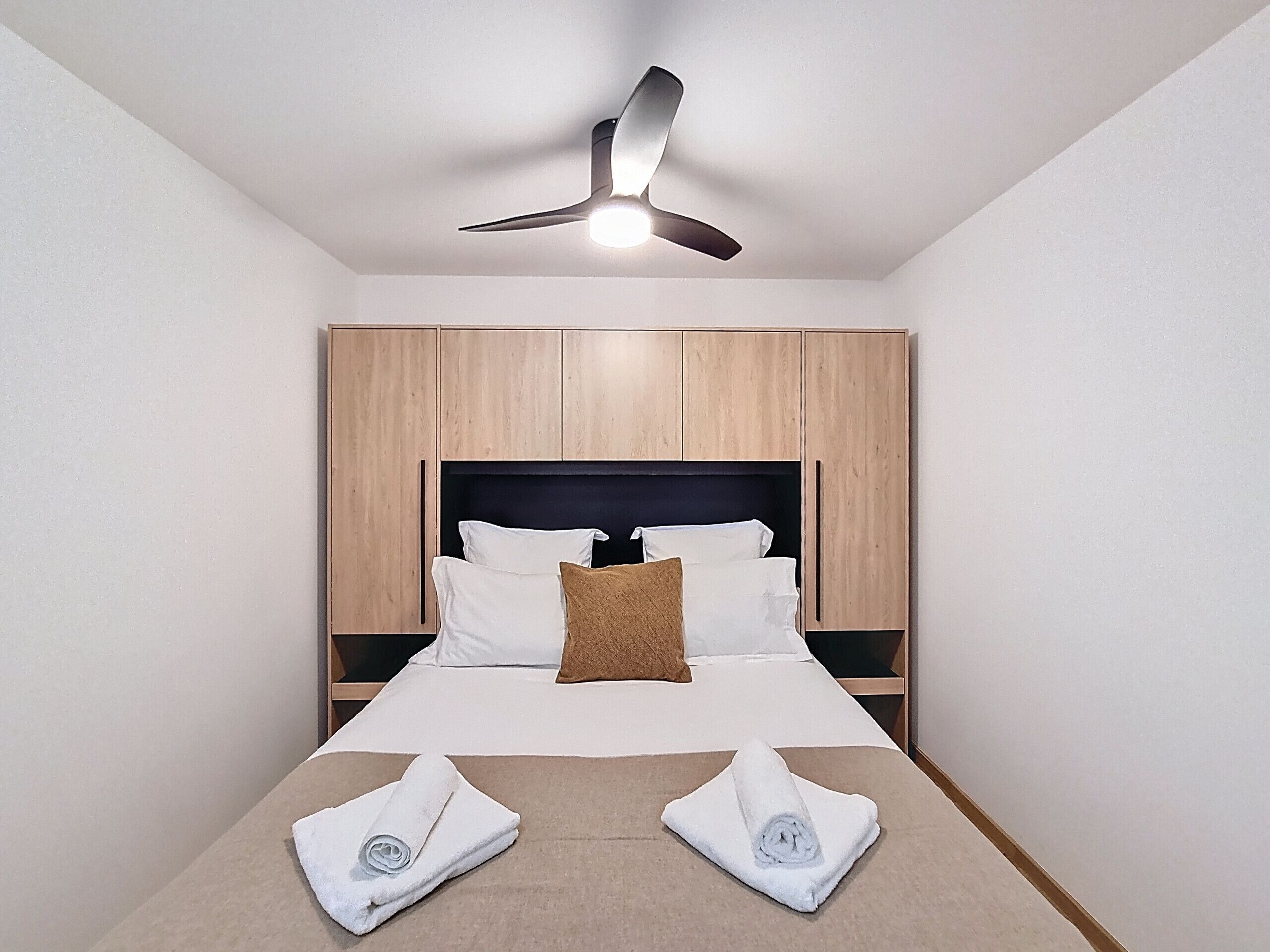 Ein Hotelzimmer mit Bett, Holzschrank, Deckenventilator und zwei Handtüchern auf dem Bett.