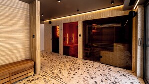 Ein moderner Wellnessraum mit einer Holzbank, einem Mosaikboden und einem Sauna Bereich.