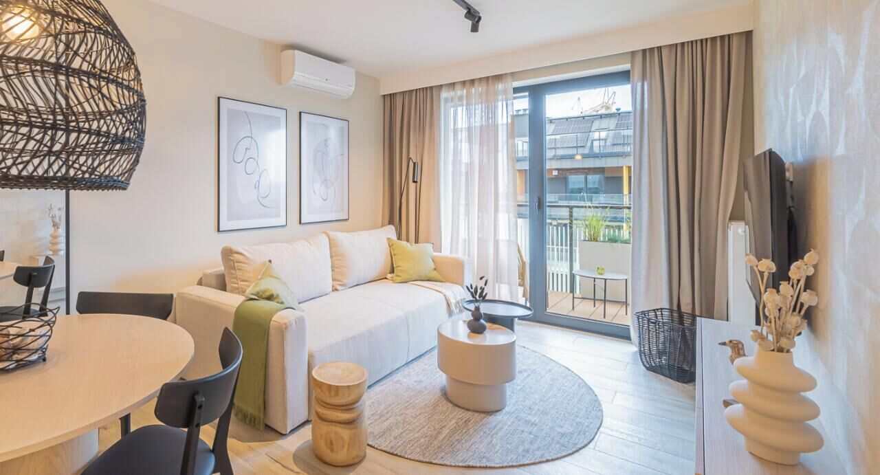 A modern hotel room with a sofa, a dining table, a round coffee table, and a large window with curtains.