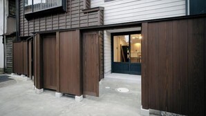 A building with a wooden exterior, a concrete ground, and a visible door leading to an interior space. - SAKON UKON (Kanazawa)