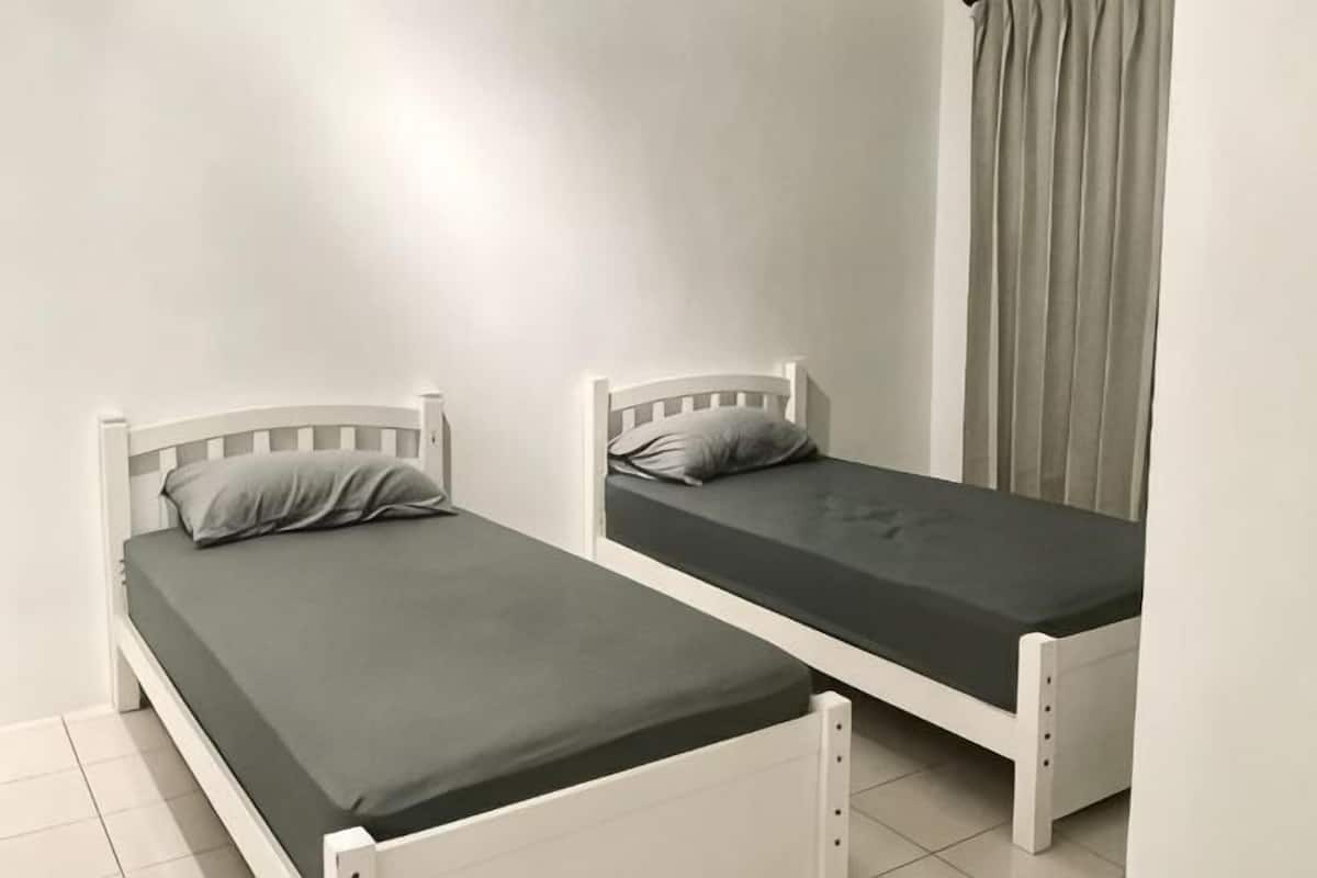 Two single beds with white frames and grey bedding in a room with white walls and a grey curtain.