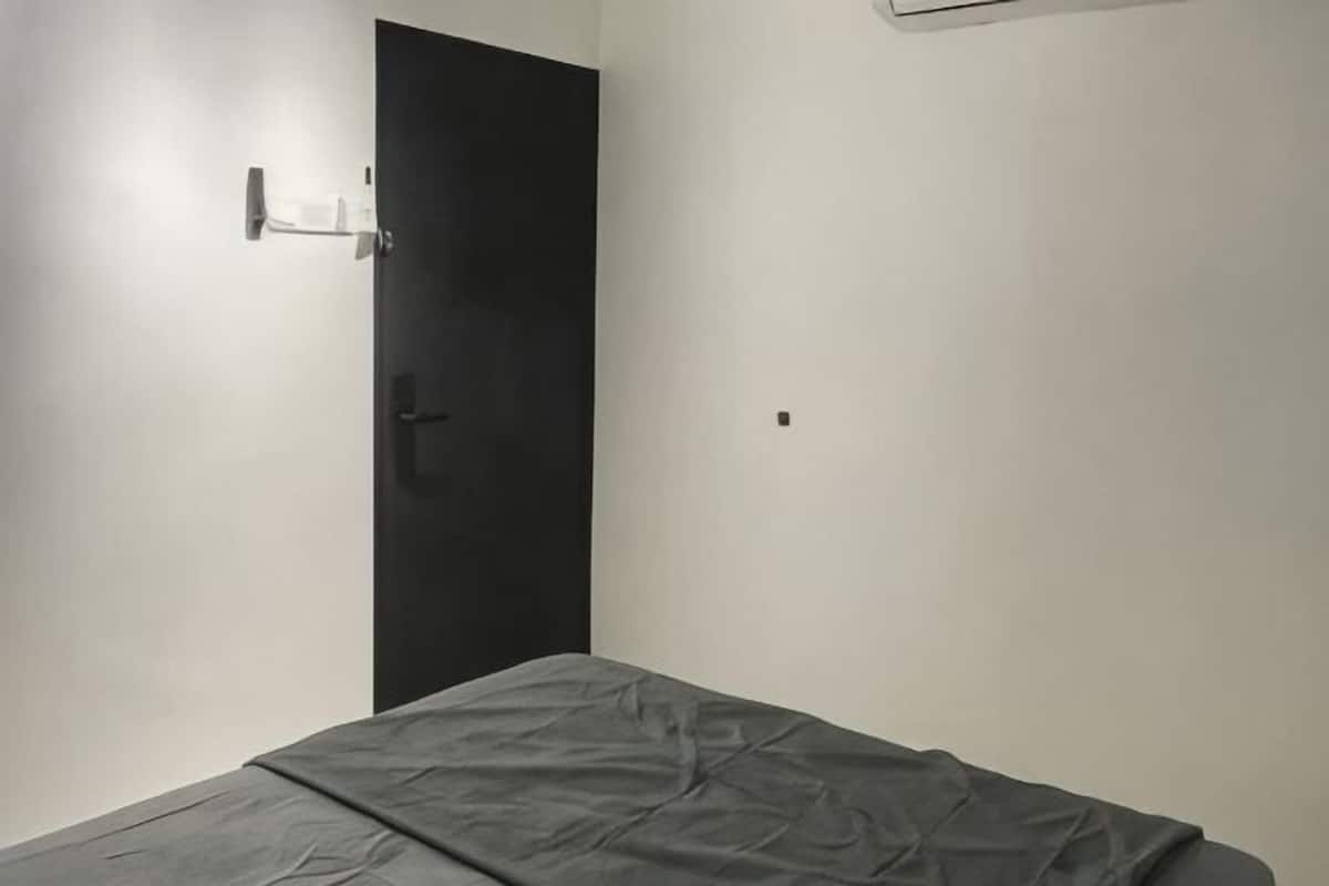 A room with a bed, a door, and a wall-mounted light fixture.