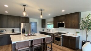 Une cuisine moderne avec des meubles en bois, un îlot central doté de tabourets, des appareils en acier inoxydable et un éclairage suspendu.
