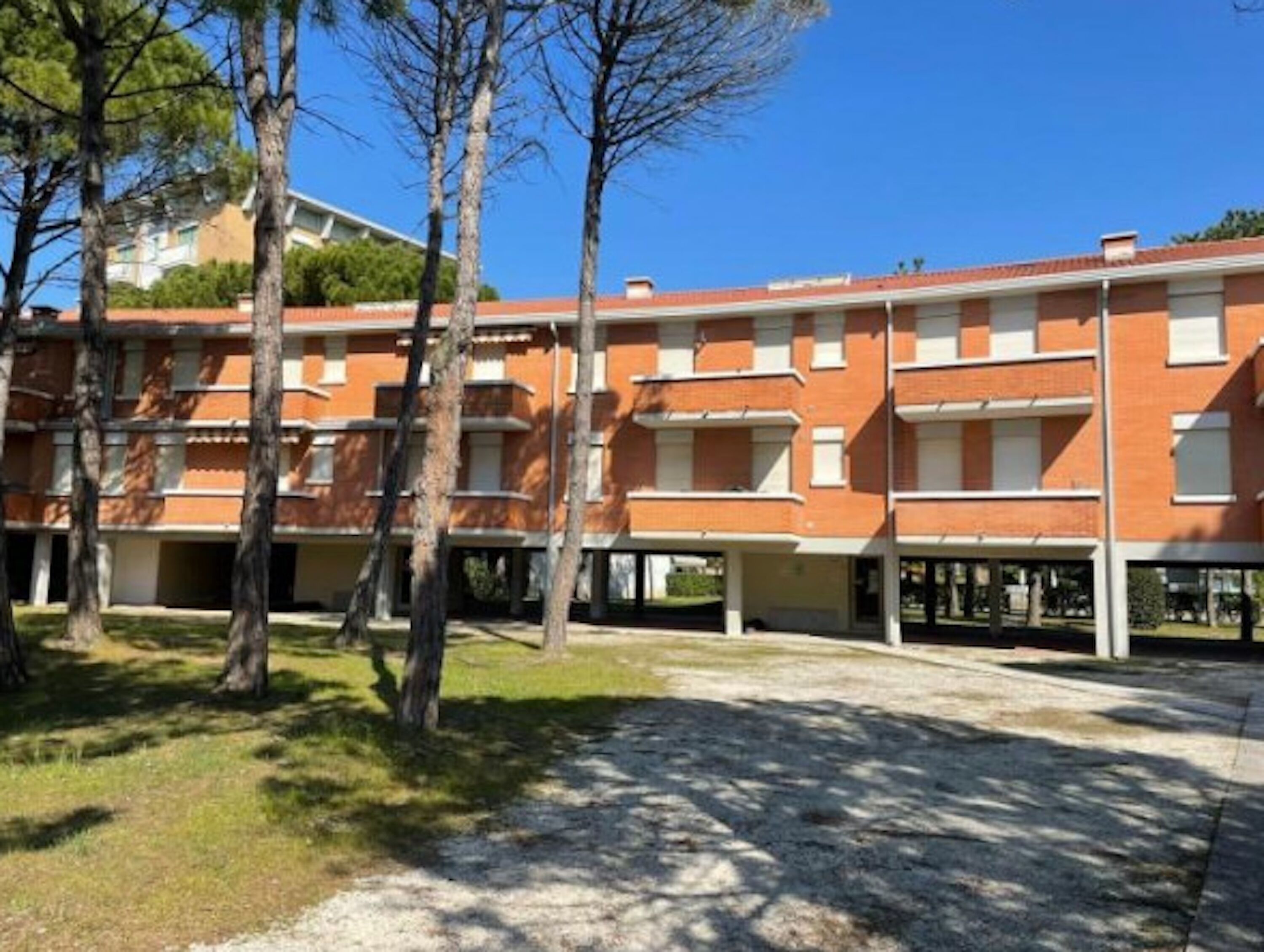 A multi-story building with a brick facade, multiple balconies, and a surrounding grassy area with trees.