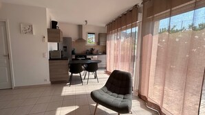 A modern kitchen with a dining area, a large window with curtains, and a chair in the foreground. - Apartment Saint-Clair (Le Lavandou) with private pool and garden - beach 300 m away (Le Lavandou)