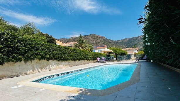 A swimming pool with a tiled deck, surrounded by greenery and hills in the background. - Apartment Saint-Clair (Le Lavandou) with private pool and garden - beach 300 m away (Le Lavandou)