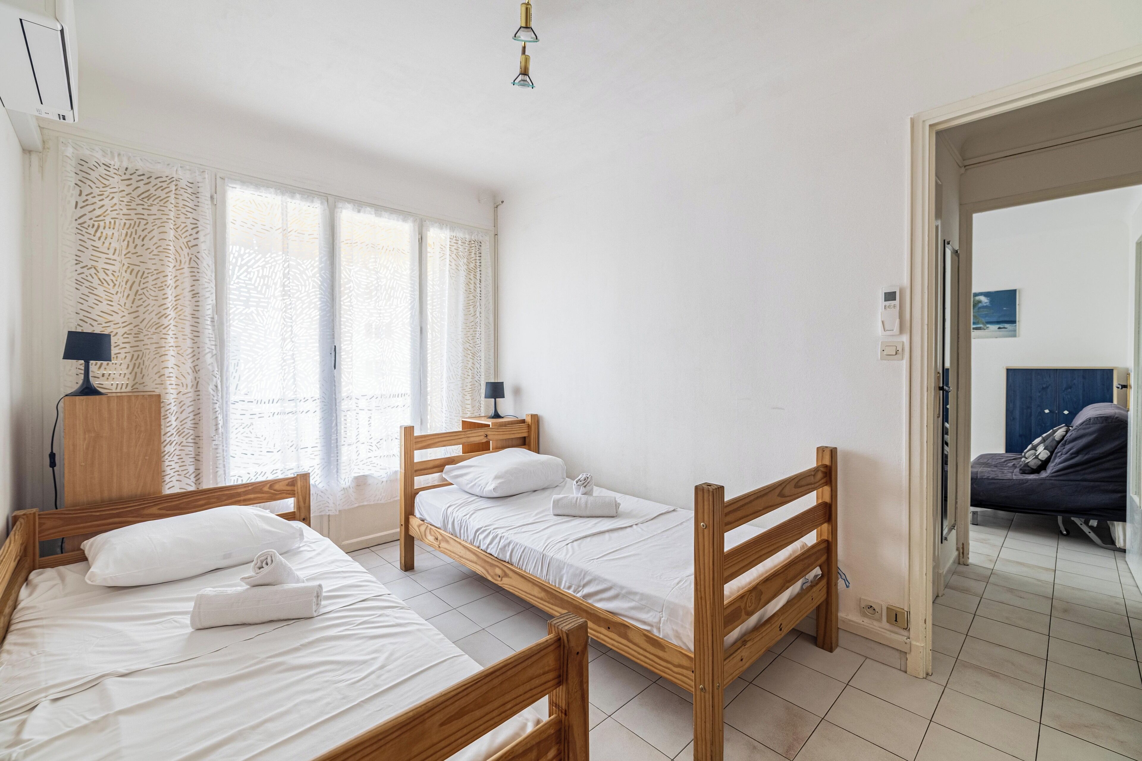 A room with three wooden beds, a desk with a lamp, and a window with patterned curtains.