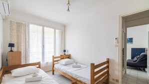 A room with three wooden beds, a desk with a lamp, and a window with patterned curtains.