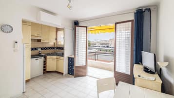 A compact kitchen with a dishwasher, a clock, and a window with curtains.