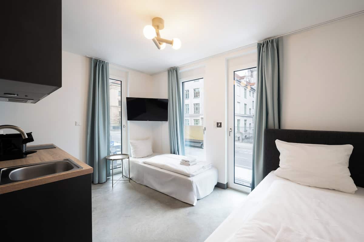 A modern hotel room with a kitchenette, a bed, a TV, and a view of the city.