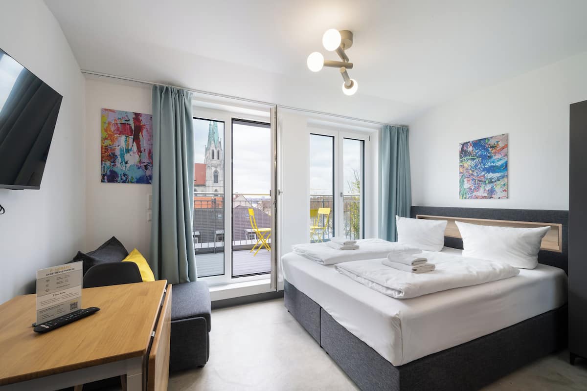 A hotel room with a bed, a desk, a chair, a TV, and a view of a building through the window.