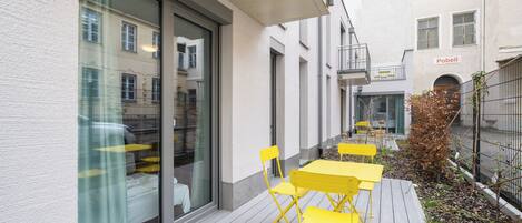 Un patio con sillas y mesas amarillas, un pequeño árbol y un edificio con un cartel que dice 'Pobell'.