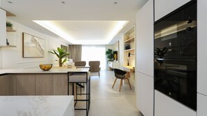 A modern kitchen with a marble countertop, wooden cabinets, and a built-in oven. There is a dining area with a table and chairs, and a plant on the counter. - Brand-new luxury with sea view  - Playa Real beachfront (Marbella)