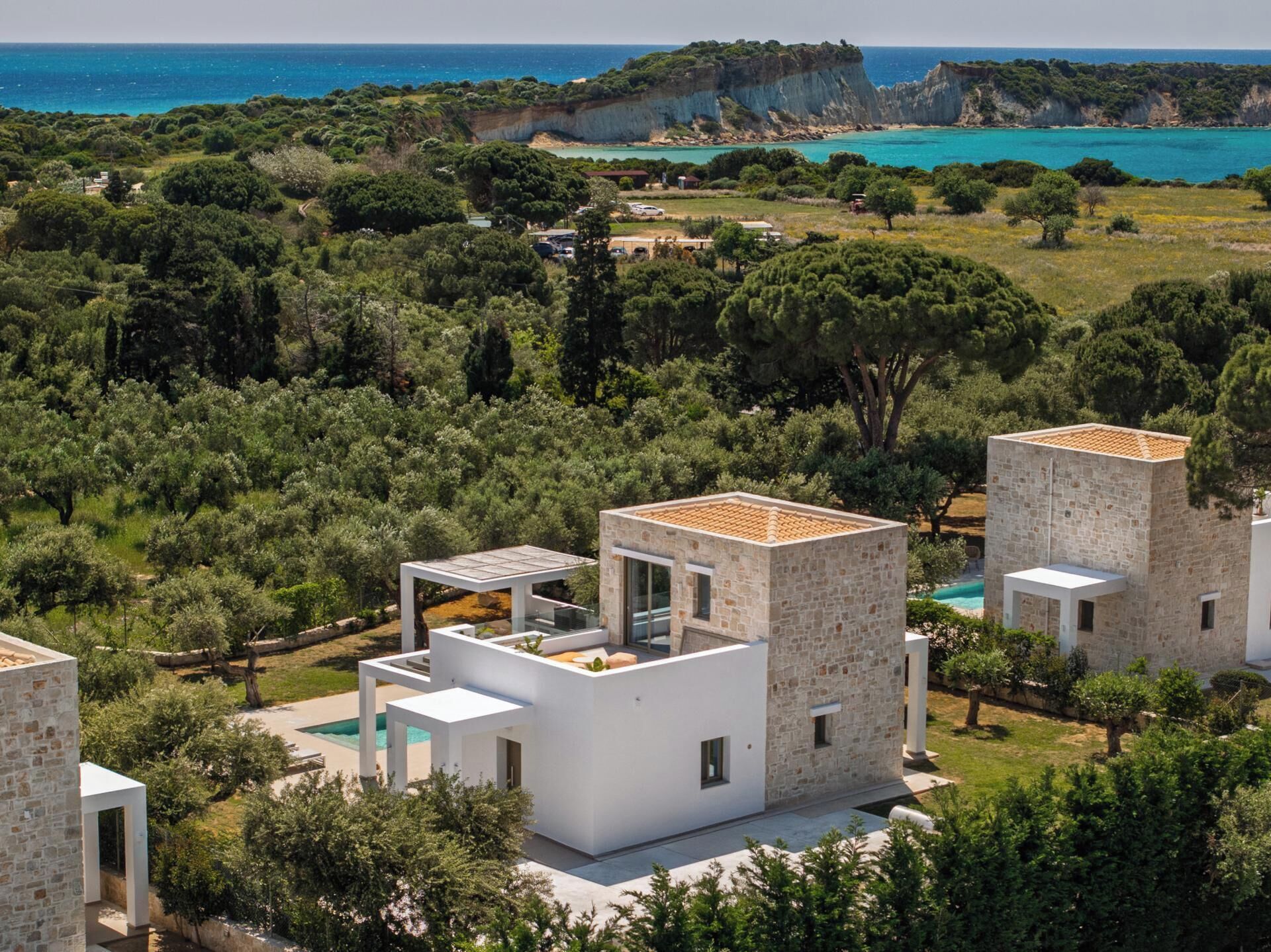 A modern villa with a pool, surrounded by lush greenery and a cliff overlooking the sea.