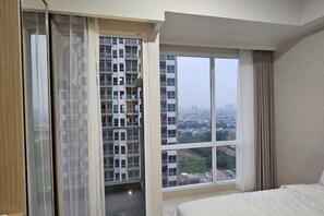 A hotel room with a large window, a bed, and a view of a cityscape. - Green Sedayu Apartment Suite by Ellison (West Jakarta)