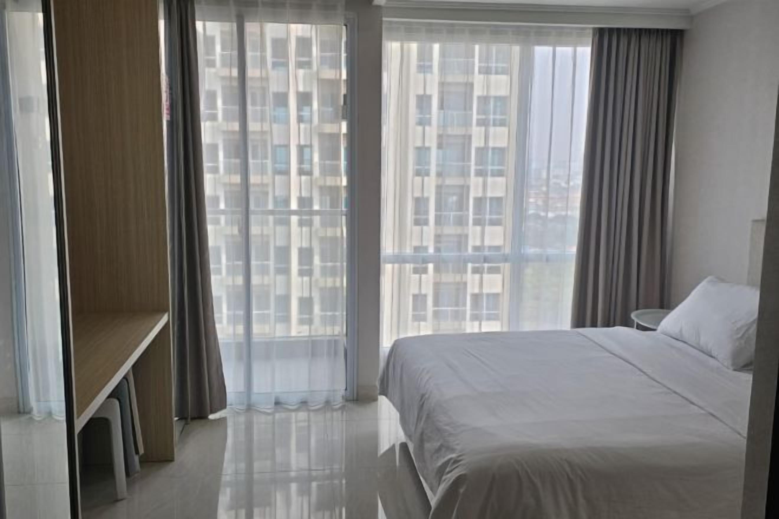 A hotel room with a large bed, a desk, and a view of buildings through sheer curtains.