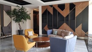 Eine moderne Lobby mit einem blauen Sofa, gelben Stühlen, einem runden Tisch und einer großen Topfpflanze.