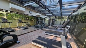 Ein Fitnessstudio mit Laufbändern, Ergometer und Gewichten, unter einer Glaskuppel mit Blick auf Grünflächen.