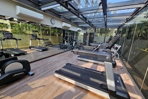 A gym with treadmills, exercise bikes, and weights, under a glass ceiling with a view of greenery.