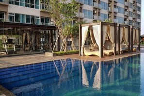 Una piscina con plataforma de madera y zona de estar cubierta.