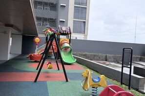 A children's play area with a slide, swings, and a climbing structure. - Green Sedayu Apartment Suite by Ellison (West Jakarta)