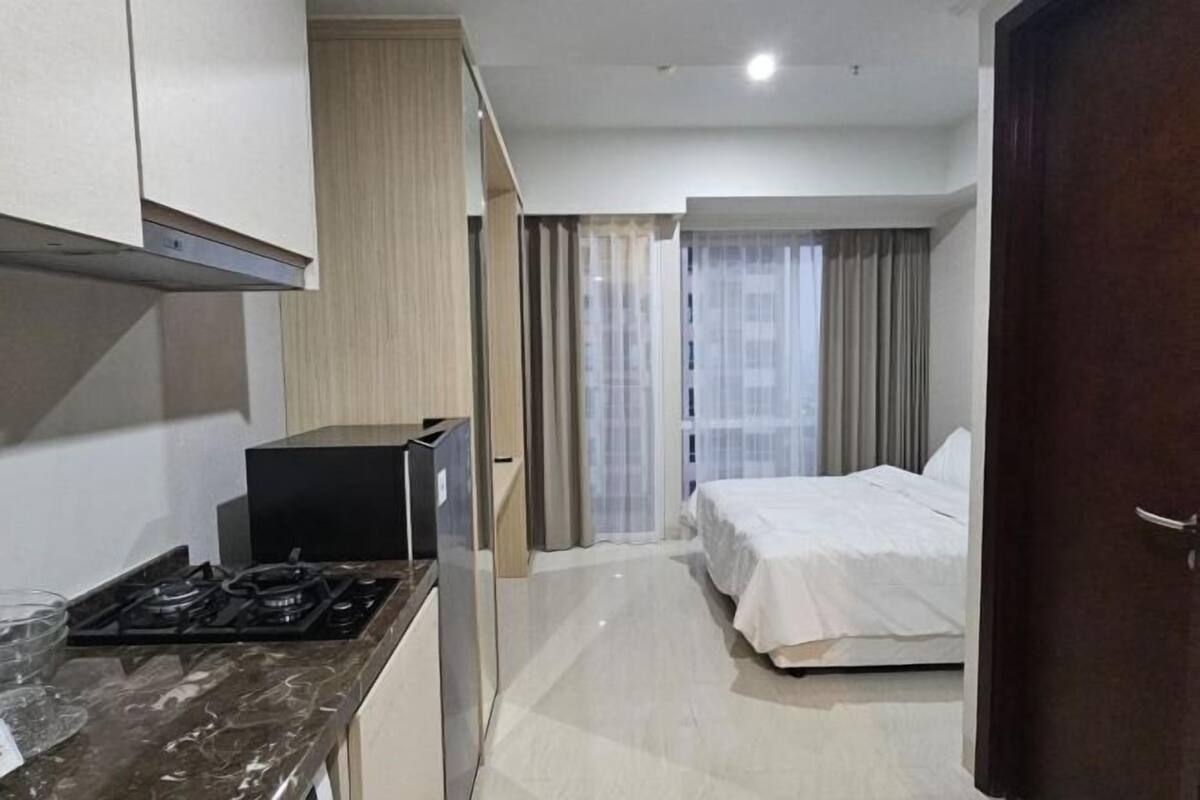 Habitación de hotel compacta con kitchenette, una cama y vistas a través de una ventana con cortinas.