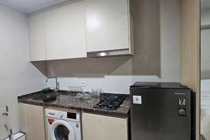 A compact kitchen with a washing machine, a refrigerator, and a stove. - Green Sedayu Apartment Suite by Ellison (West Jakarta)