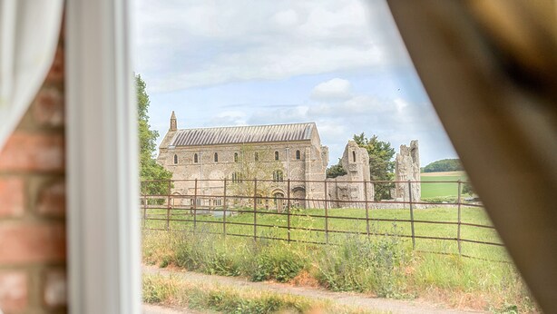 Een historisch gebouw met een groot stenen bouwwerk en een kleinere toren, zichtbaar door een raam met een metalen hek voorop.