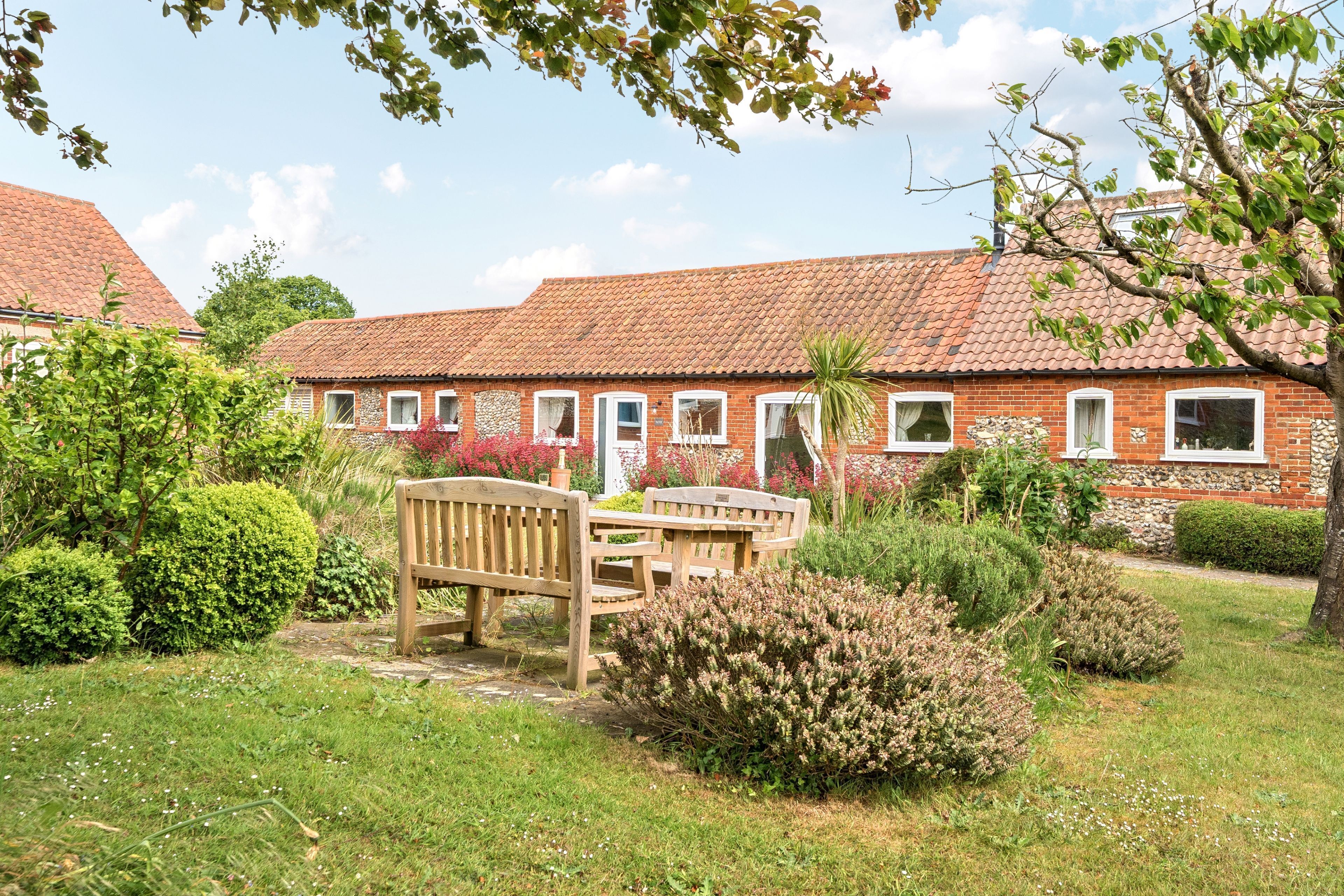 A brick building with a tiled roof, surrounded by well-maintained gardens and a wooden bench.
