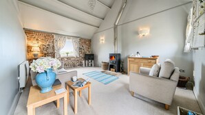 Een gezellige woonkamer met een stenen muur, een open haard, een bank en een eethoek met een tafel en stoelen.