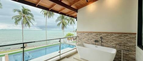 A modern bathroom with a freestanding bathtub, a stone accent wall, and a view of the ocean.