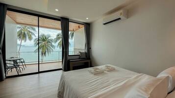 Un dormitorio con cama, escritorio y vista a palmeras y al mar.