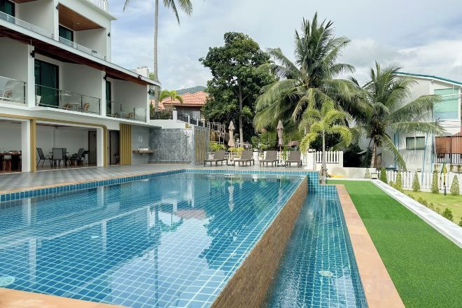 A swimming pool with a tiled edge, surrounded by a grassy area and palm trees.