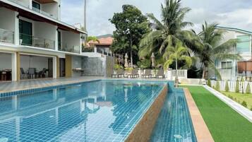 Piscina com borda azulejada, cercada por gramado e palmeiras.