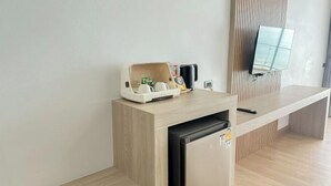 A modern room with a wooden desk, a small refrigerator, a coffee maker, and a television mounted on the wall.