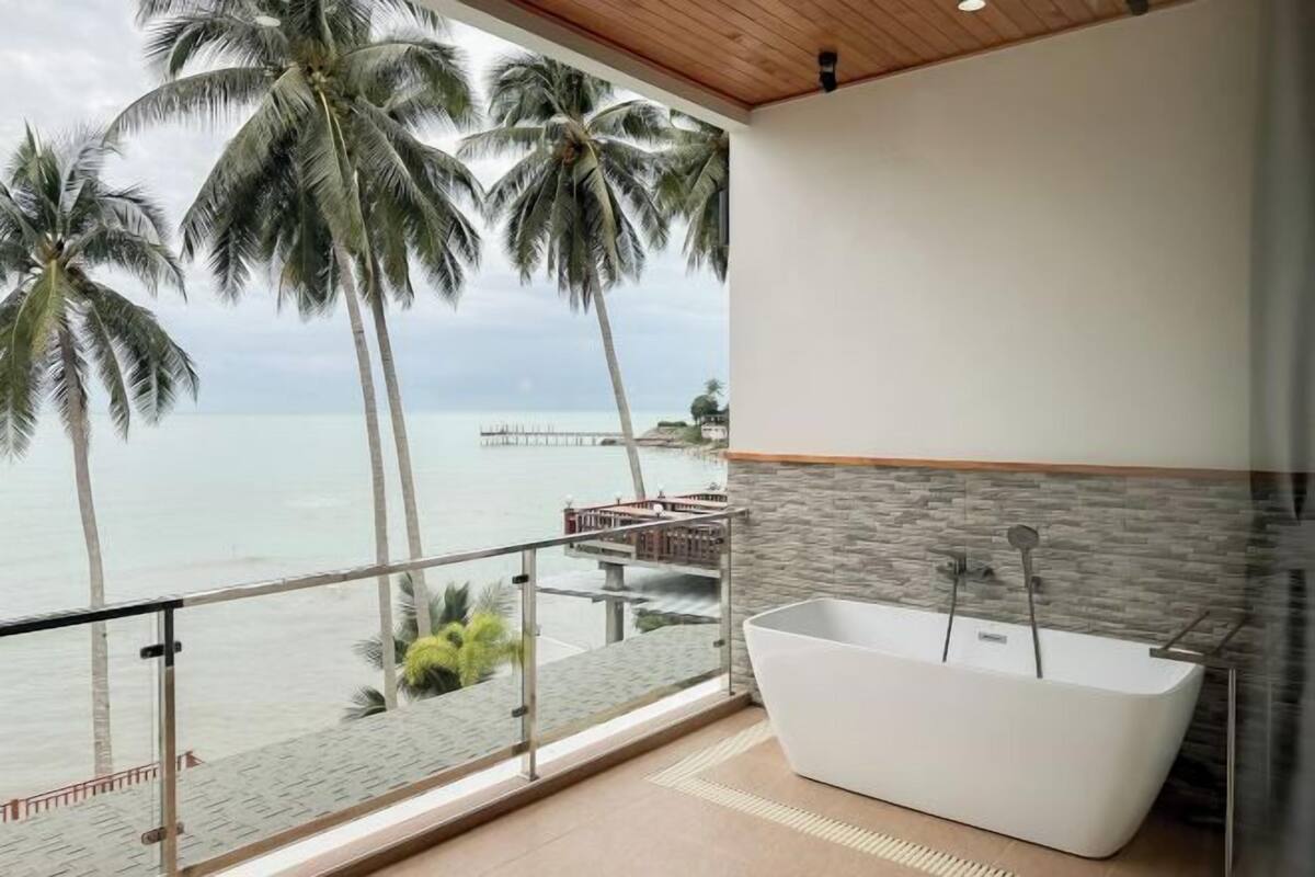 Une salle de bain moderne avec une baignoire, une vue sur la mer et des palmiers.
