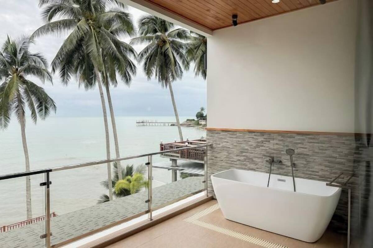 Une salle de bain moderne avec une baignoire sur pieds, un mur en pierre et une vue sur l’océan et les palmiers.