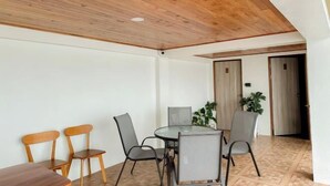 A dining area with a round table and chairs, wooden ceiling, and a door leading to another room.