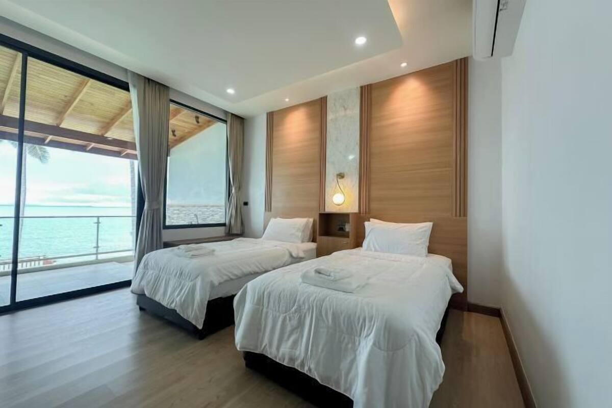 Une chambre d’hôtel avec deux lits, une grande fenêtre donnant sur la mer et un plafond en bois.