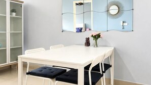 A dining area with a white table, four chairs, a vase with flowers, and a wall-mounted decorative panel.