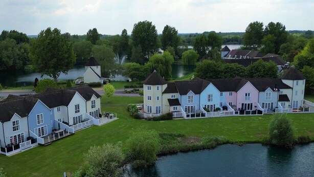 A row of pastel-colored houses with a river in the foreground. - Windrush Lake 20, Summit Lodge (P) - Lakeside Lodge, On-site Activites, Sleeps 7 (South Cerney)