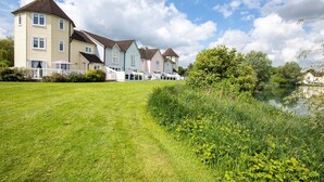 A row of traditional houses with a grassy lawn and a pond in the foreground. - Windrush Lake 20, Summit Lodge (P) - Lakeside Lodge, On-site Activites, Sleeps 7 (South Cerney)